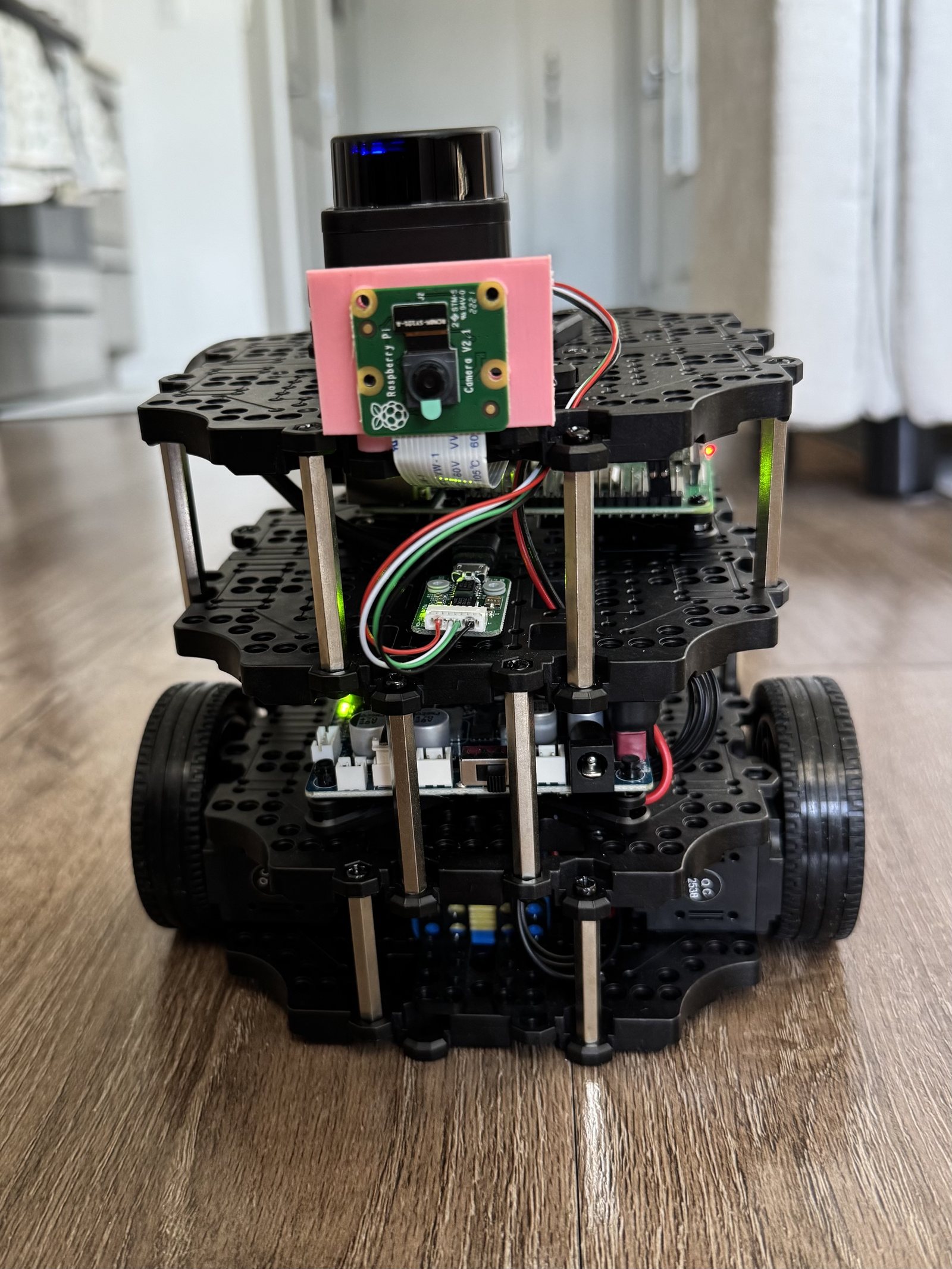 Fully assembled TurtleBot3 Burger — LiDAR unit on top, Raspberry Pi camera in a pink 3D-printed mount, stacked waffle plates with Raspberry Pi 4 and OpenCR